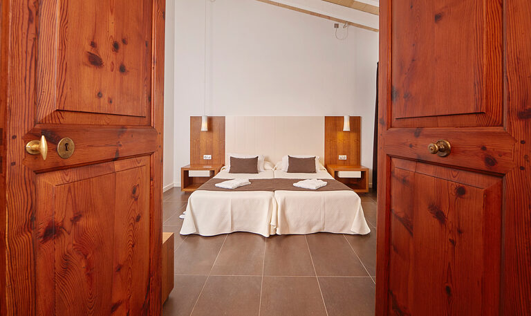A large suite under a white vaulted ceiling: a stone-clad headboard wall, a wide bed, an open bathroom and a corner whirlpool tub