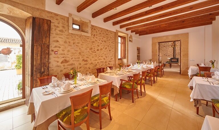 The Exquisit dining room: white-clothed tables, an exposed stone wall, a beamed ceiling and an arched doorway opening onto the courtyard